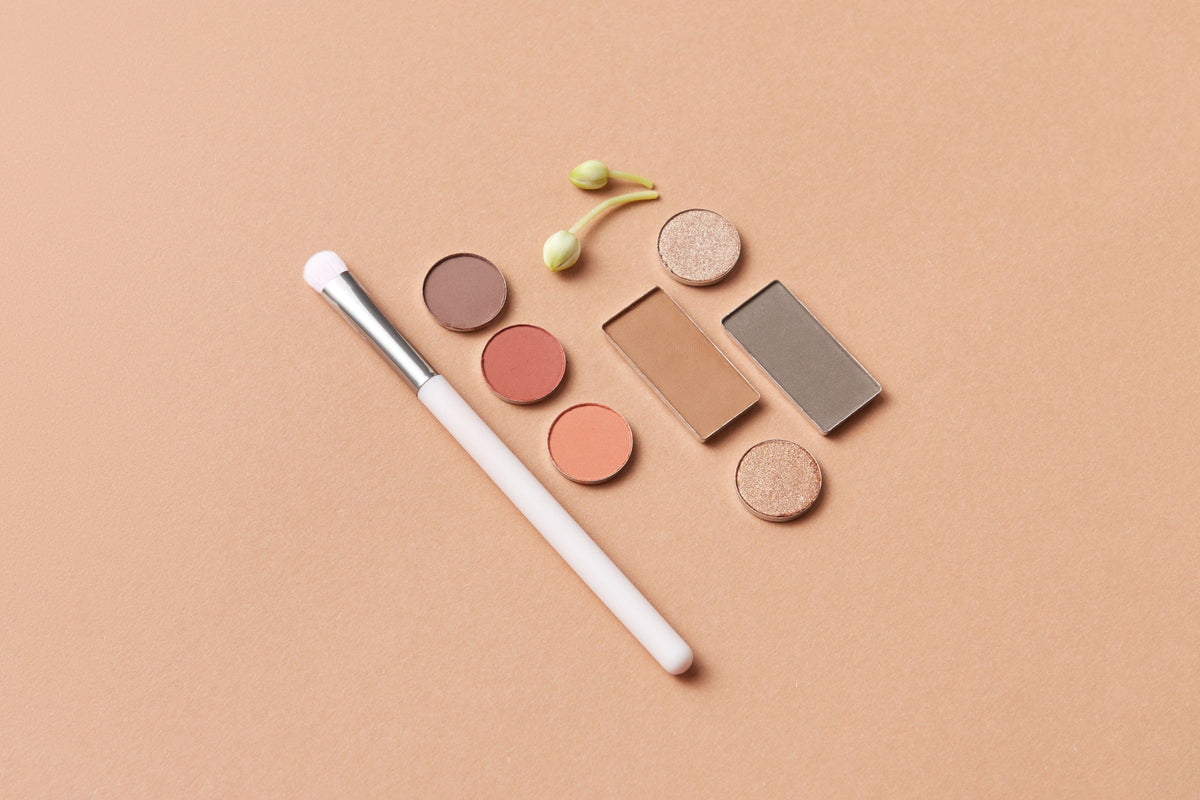 Makeup brushes, eyeshadow and a facial roller styled on a warm beige surface