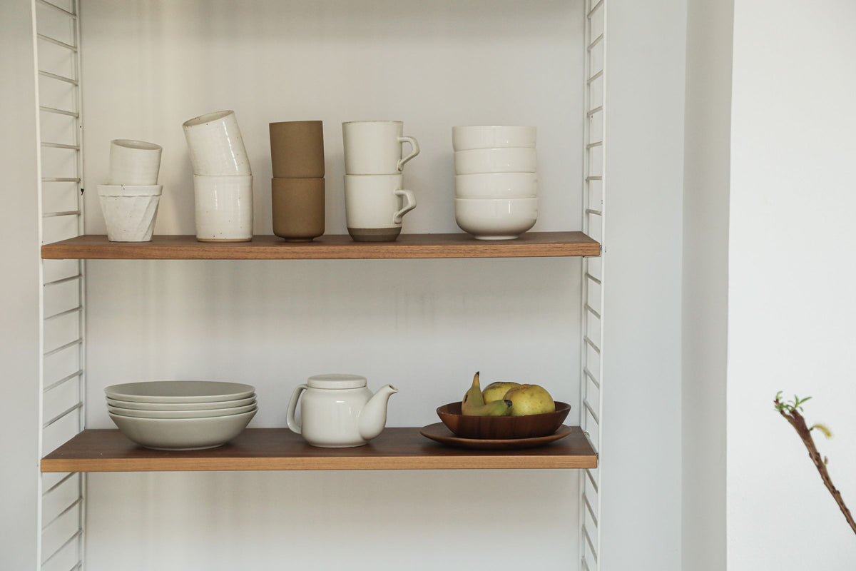 Stoneware mugs and bowls arranged on an open kitchen shelf